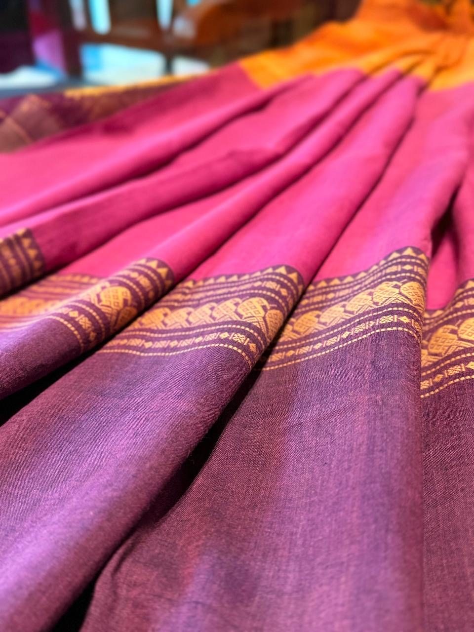 Pleats of a magenta cotton saree finished with a fine gold border