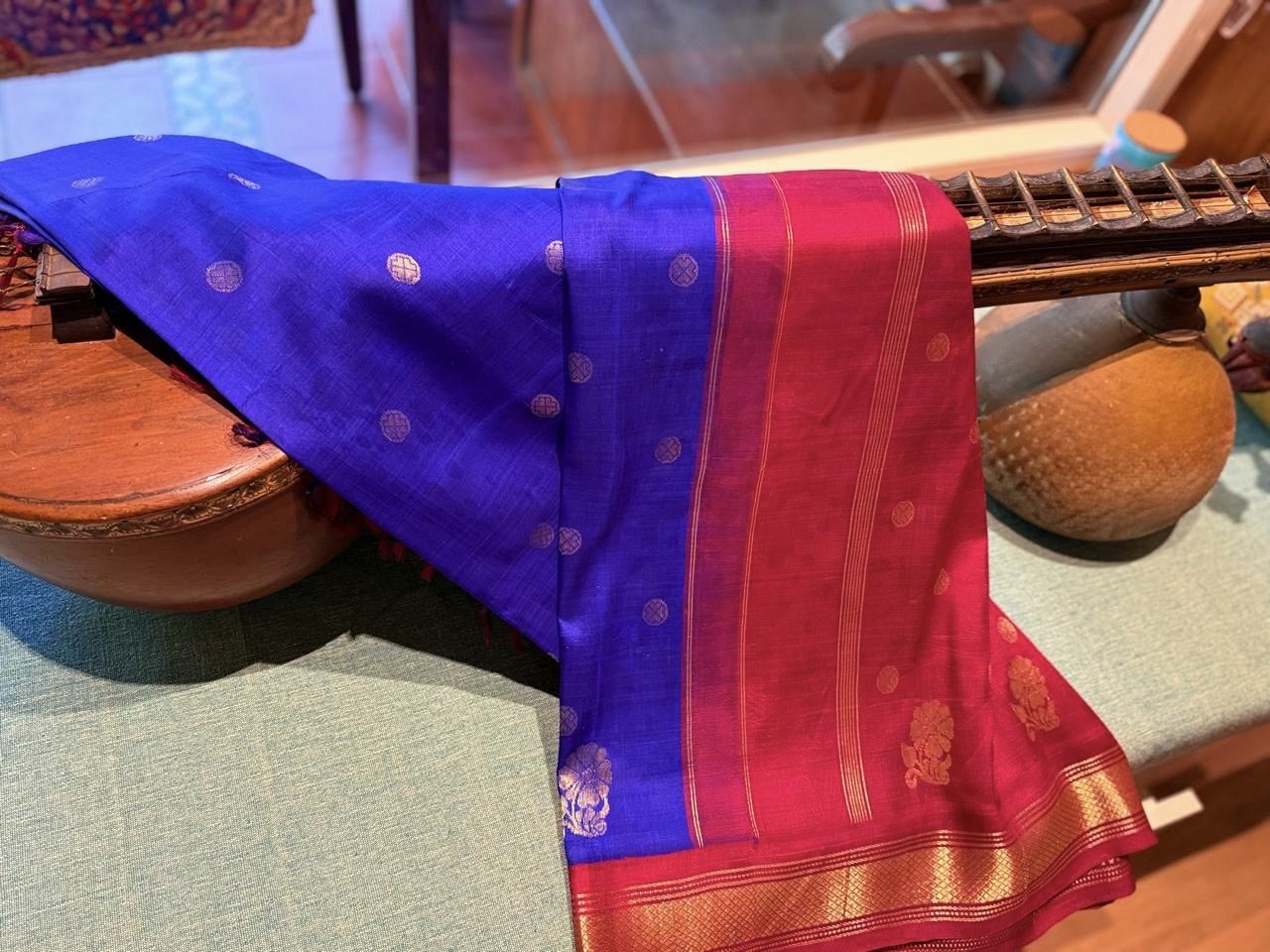 A blue silk-cotton saree with a crimson and gold border, draped over a veena