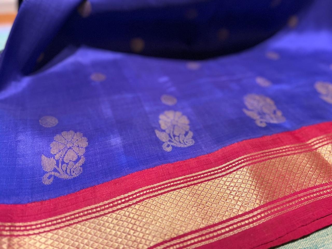 Gold floral butis on a blue saree, next to a crimson border woven with gold zari